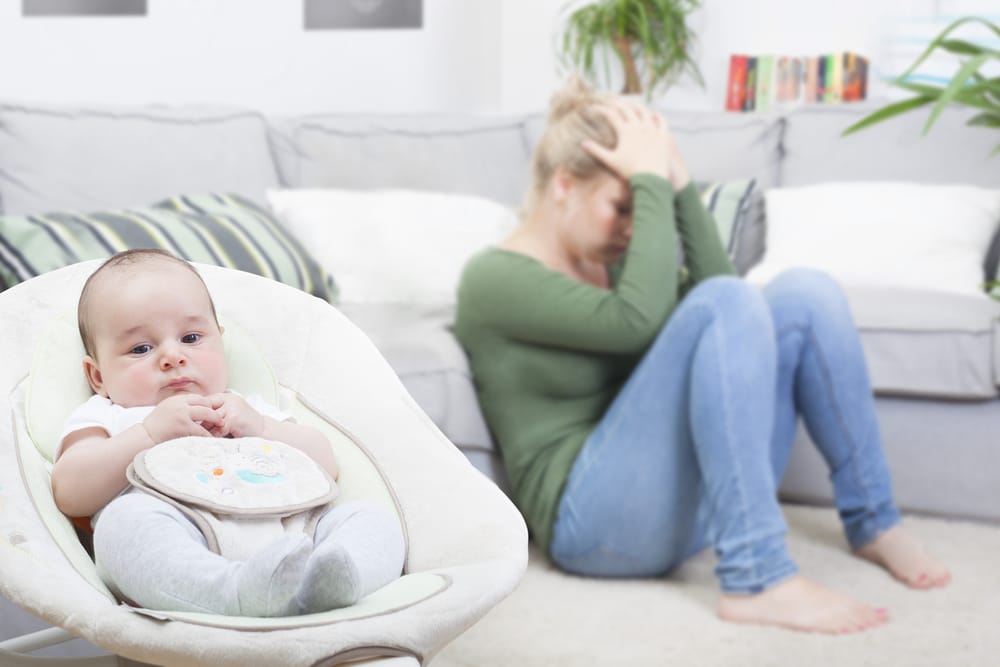 Young woman with postpartum depression, baby in rocker, woman with head in hands