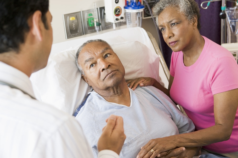 Senior couple looking concerned in hospital, man in hospital bed, talking to doctor