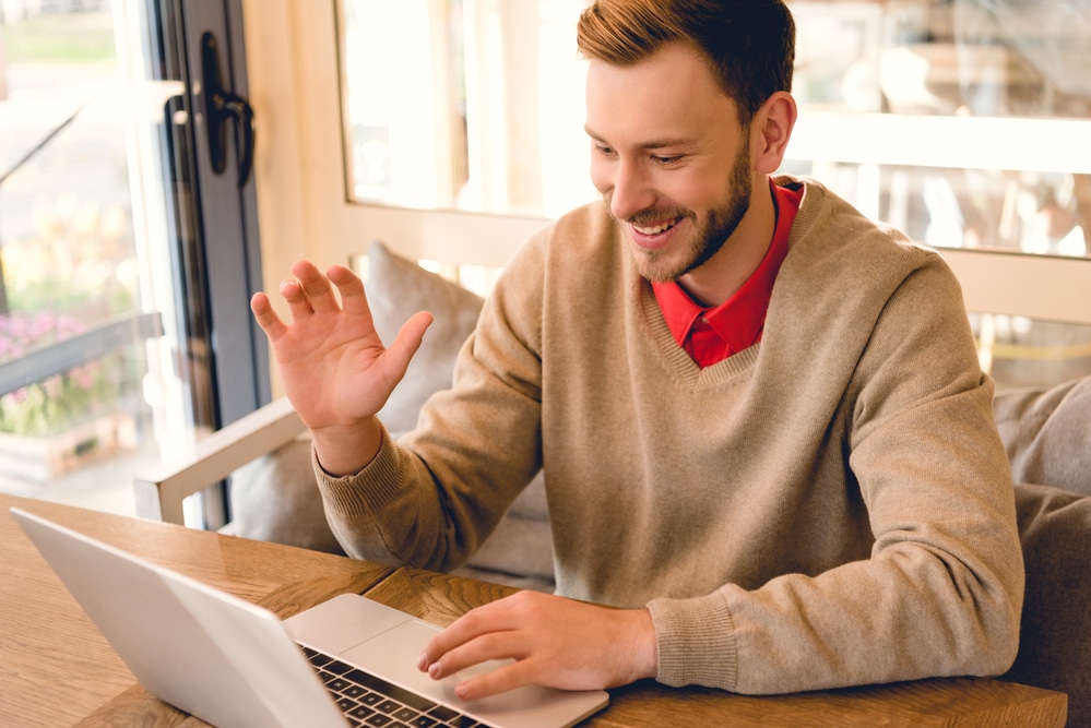 Young smiling man waving to someone over video chat on laptop