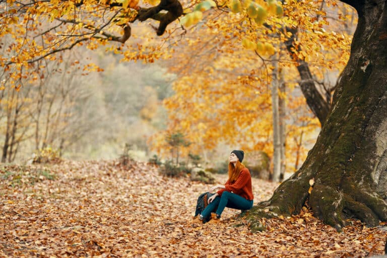 Young woman sitting beneath yellow autumnal tree looking into distance